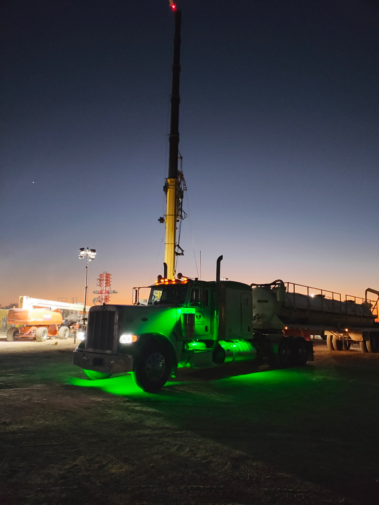 Vacuum truck working under a crane at dusk